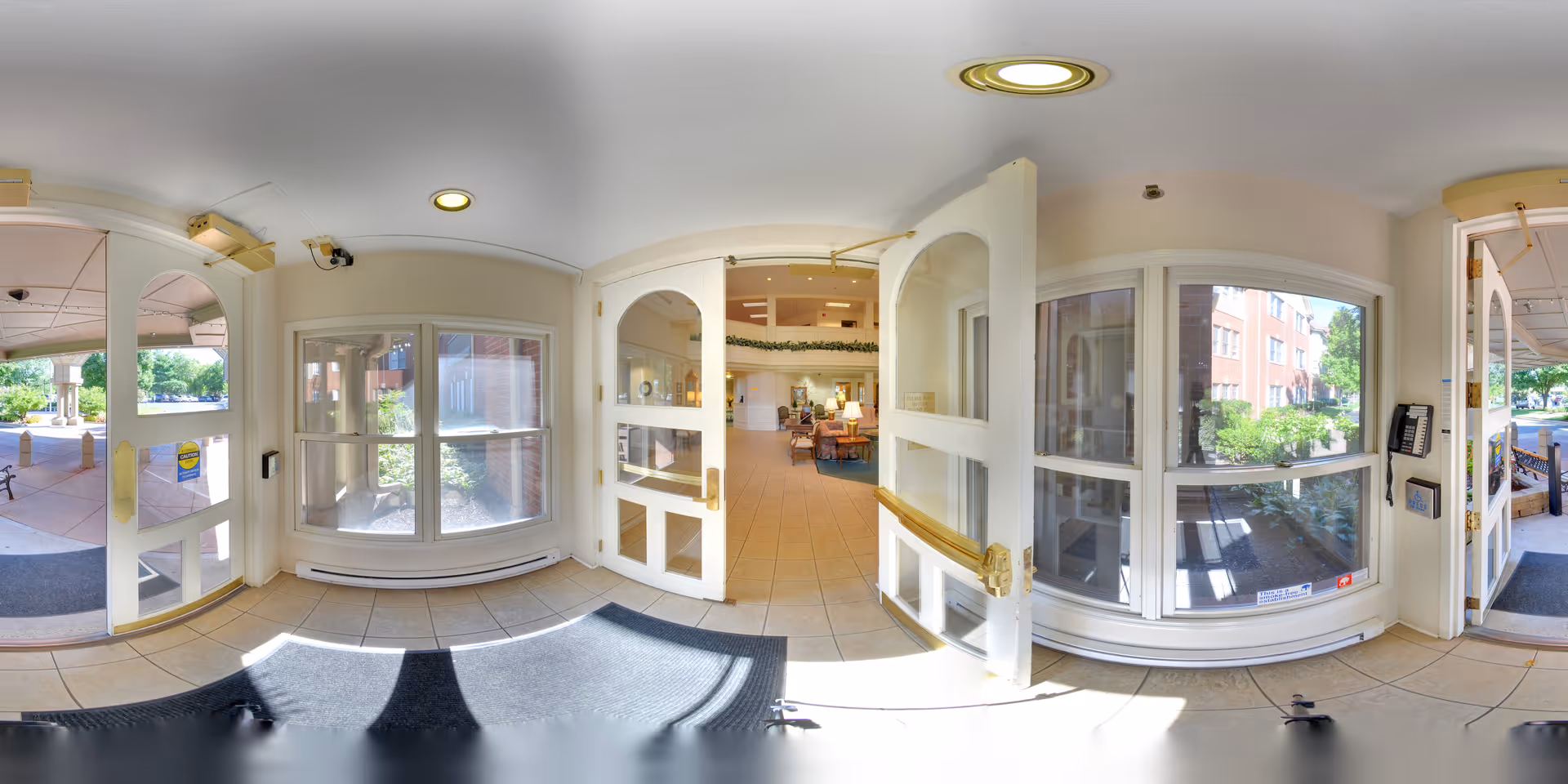 Bright tiled entrance foyer with double glass doors and large windows opening into a lobby with seating.