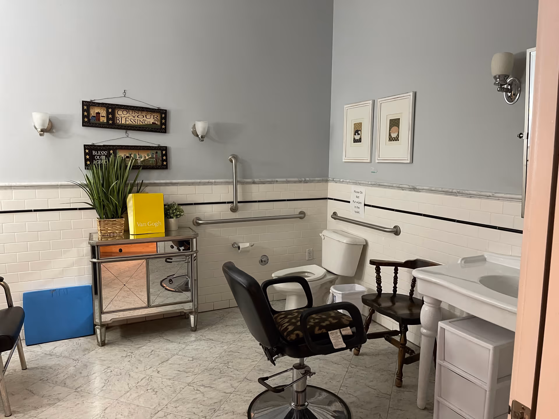 Accessible bathroom with a toilet, sink, grab bars, chairs and decorative wall art.