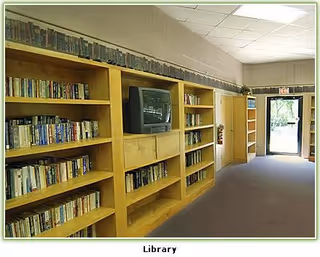 Interior library corridor with wooden bookshelves, a television on a shelf, carpeted floor, and a doorway to the outside.