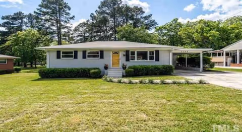 Single-story light-blue senior living home with front yard, shrubs, and carport.