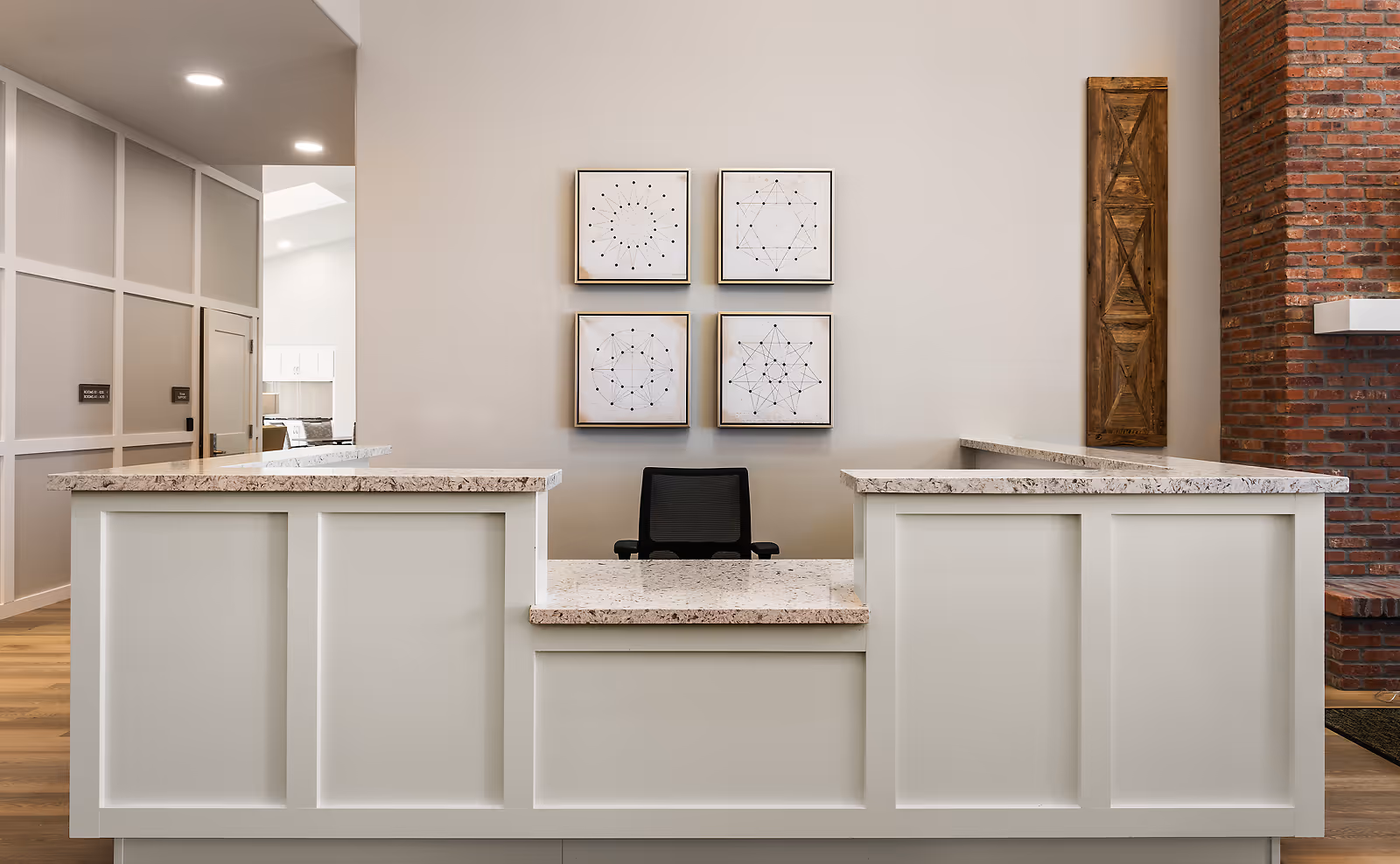 A bright reception desk inside the facility with a chair behind it, four framed geometric prints on the wall and a brick accent column.