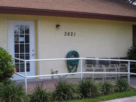 Exterior view of a beige building entrance with ramp, address 3621, coiled hose, and plants.