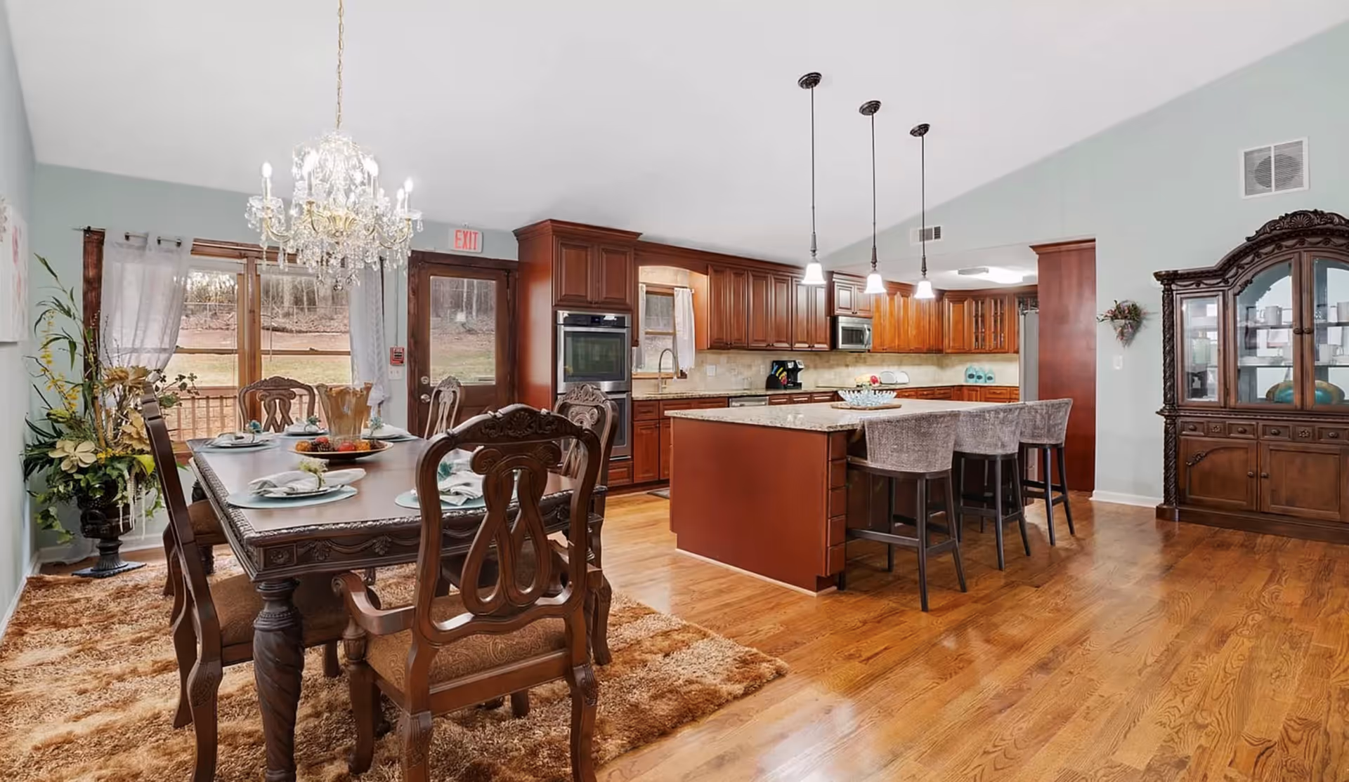 Open-concept dining area with a formal wooden dining table and chandelier adjacent to a large kitchen with an island and bar stools.