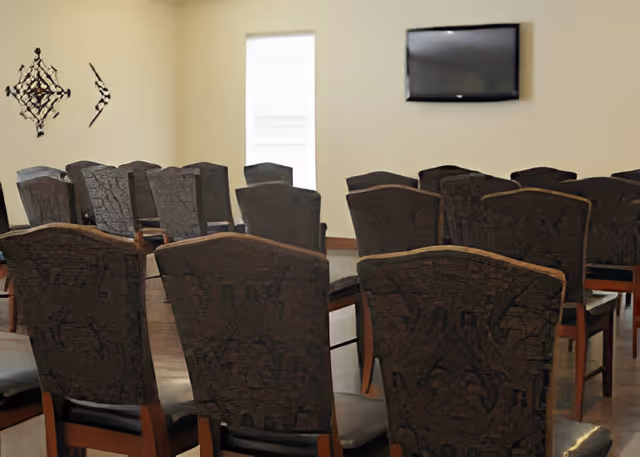 Rows of upholstered chairs arranged theater-style facing a wall-mounted television in a meeting/activity room.