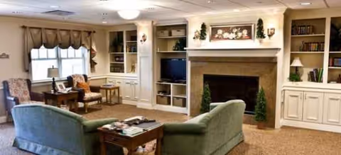 Cozy senior living room with fireplace, built-in shelves, and cushioned seating.