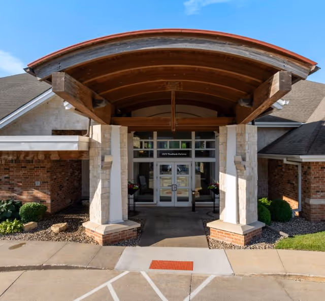 Entrance to Woodlands Creek senior living facility featuring a curved wooden canopy and glass doors.