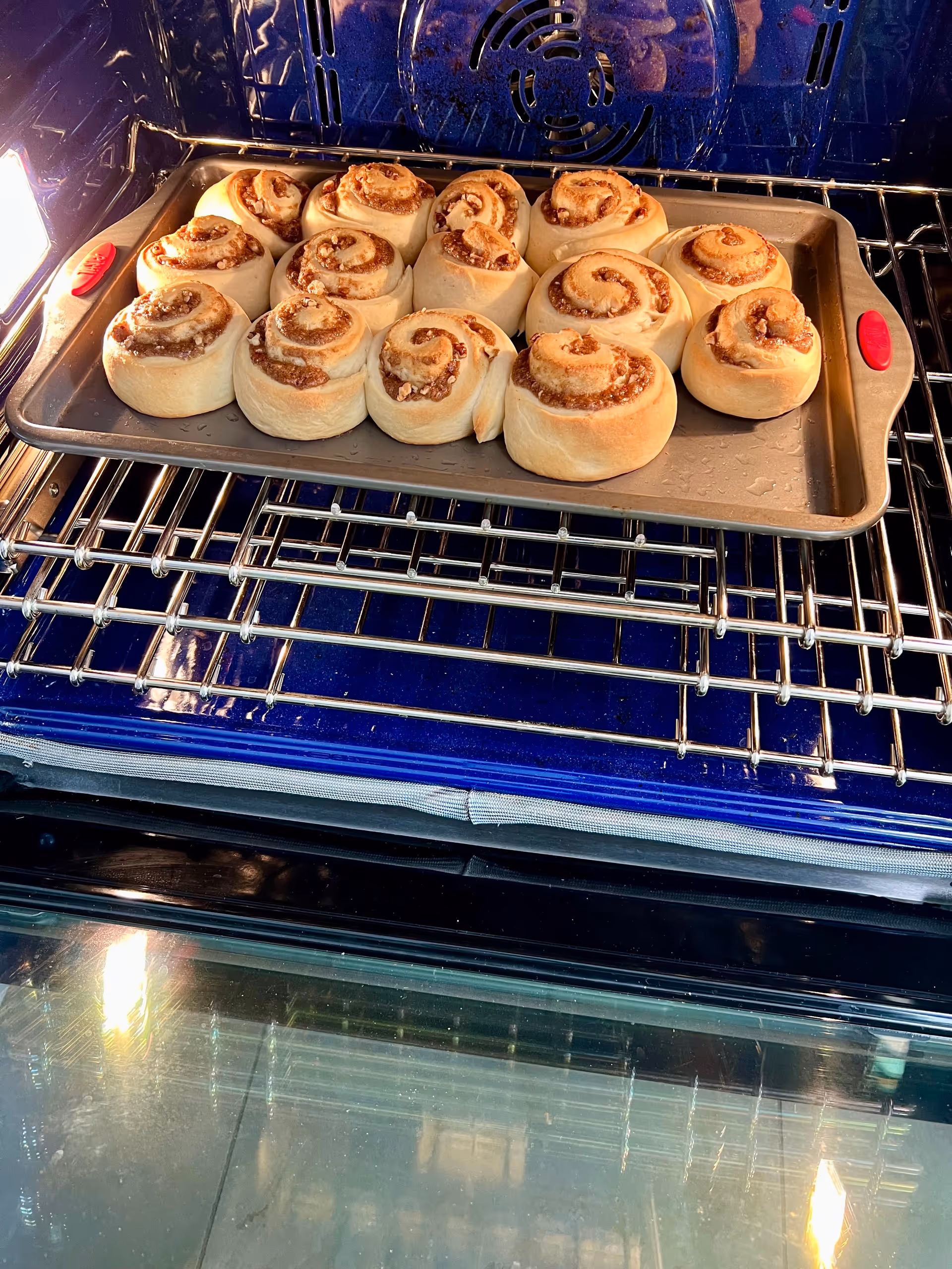 A tray of cinnamon rolls baking inside an oven with a blue interior and metal racks.