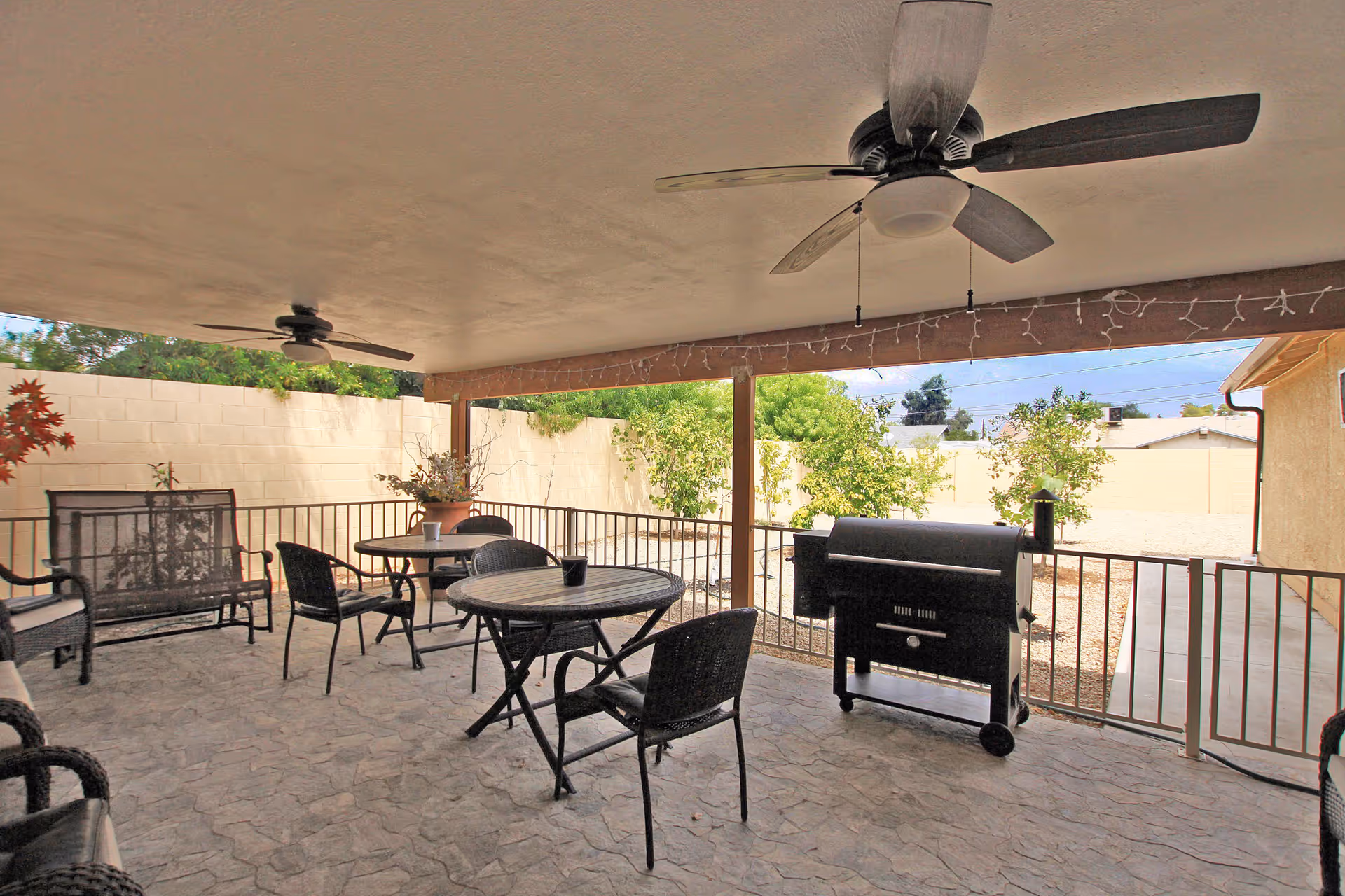 Covered outdoor patio with round tables, chairs, ceiling fans, and a barbecue grill.