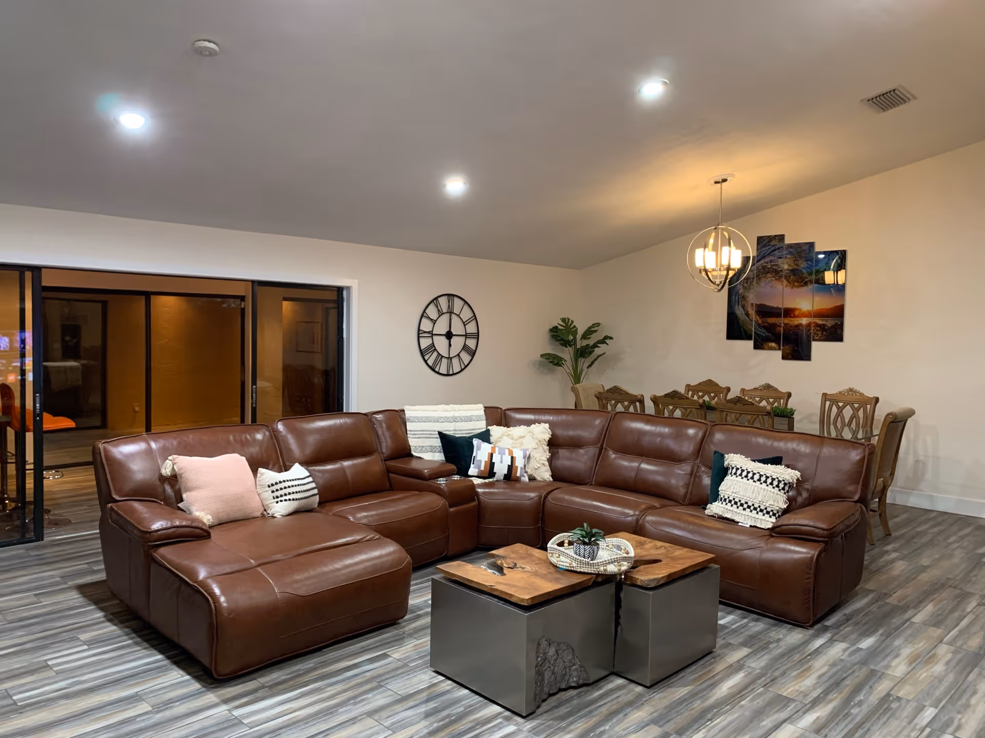 Spacious open living area with a brown leather sectional sofa, coffee tables, and a dining table in the background.