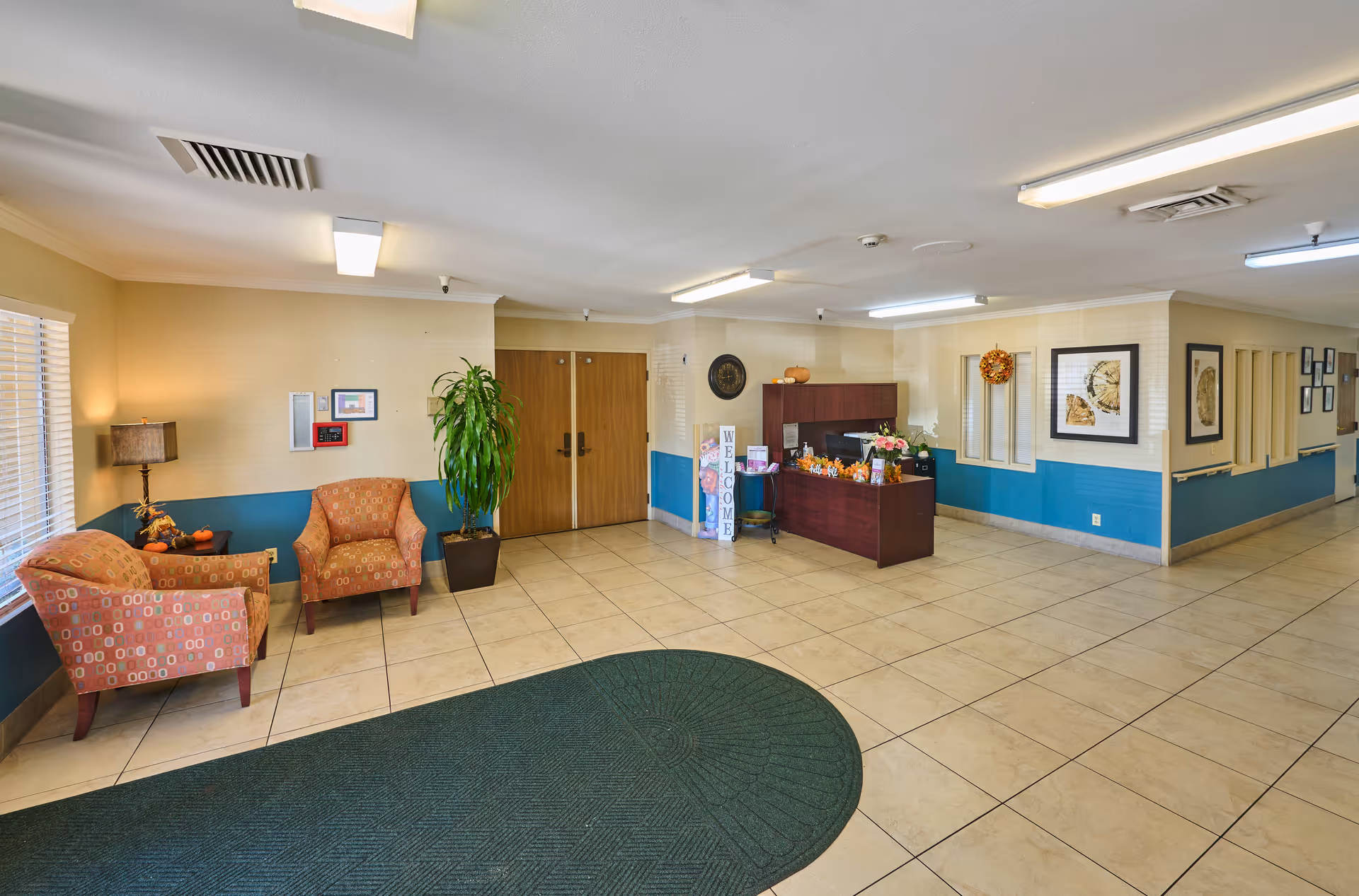 Reception lobby of a nursing and rehabilitation center with seating, a front desk, potted plant and double doors.
