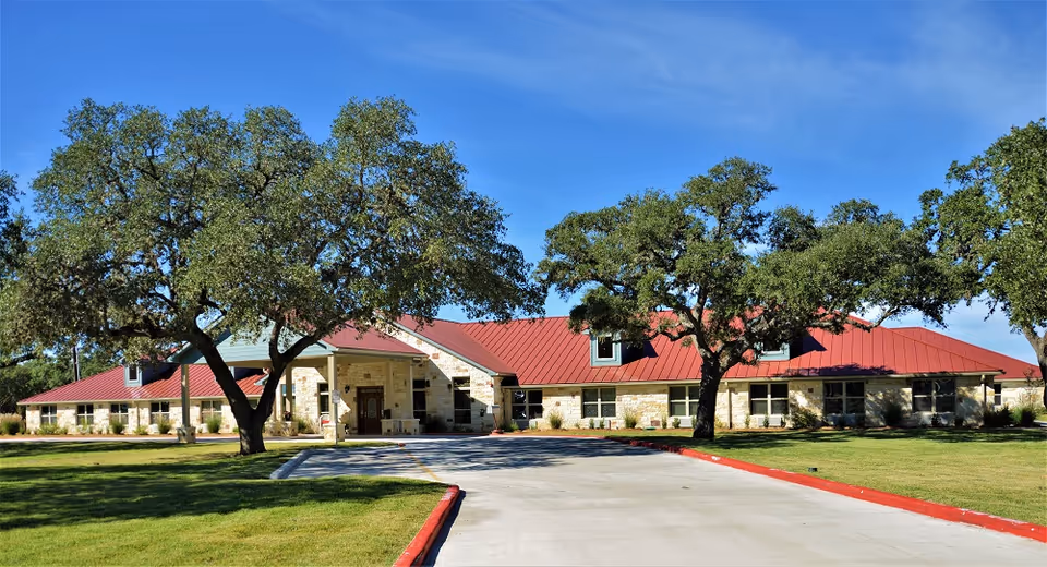 Exterior view of a stone senior living facility with a red roof and trees.