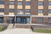 Exterior view of a multi-story brick building with a sign above the entrance that reads 'West Lawrence Care Center'. The entrance has double glass doors and is accessed by stairs and a ramp with metal railings. The building has several windows and a concrete sidewalk in front.