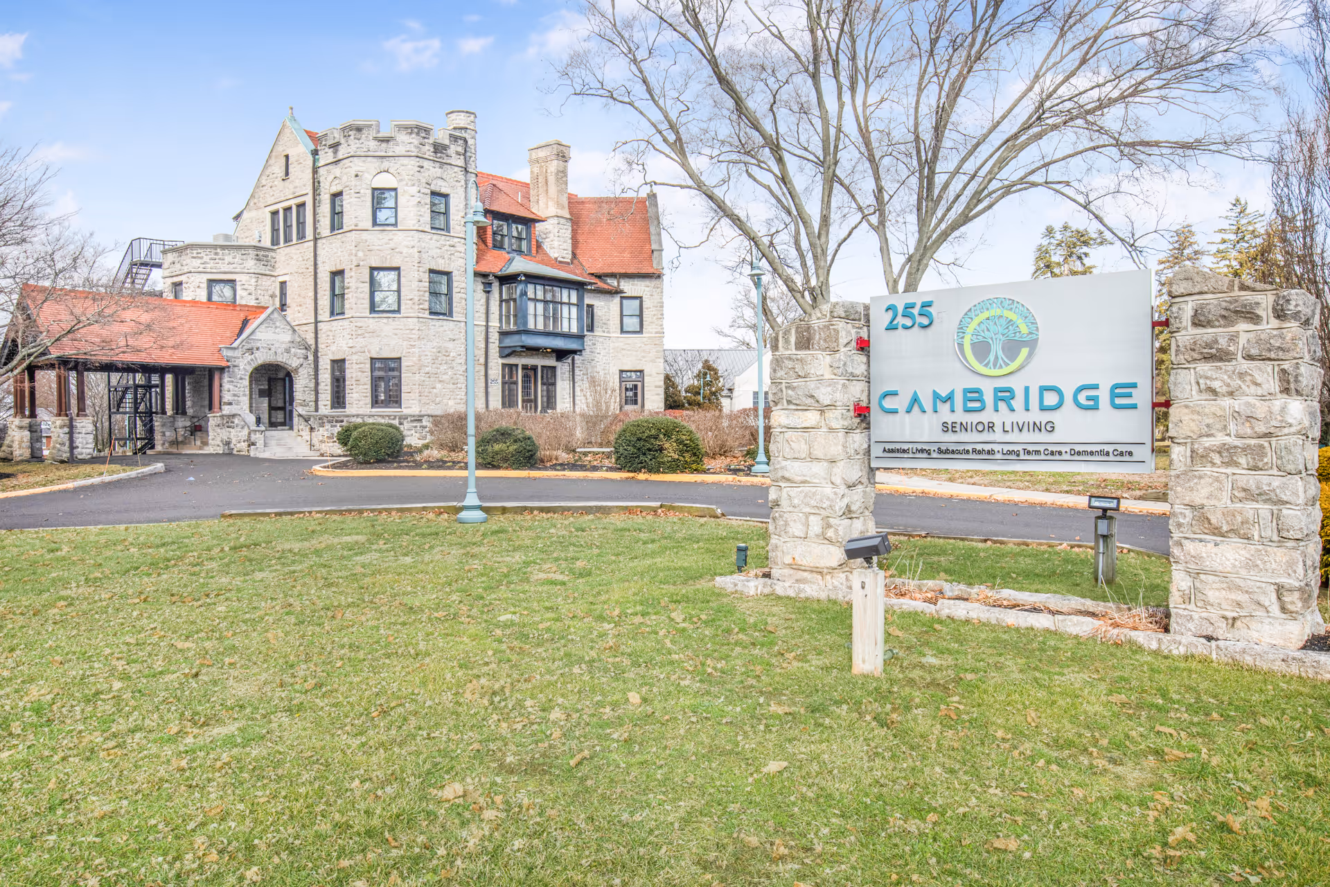 Stone mansion-style senior living building with a lawn and a prominent 'Cambridge Senior Living' entrance sign.