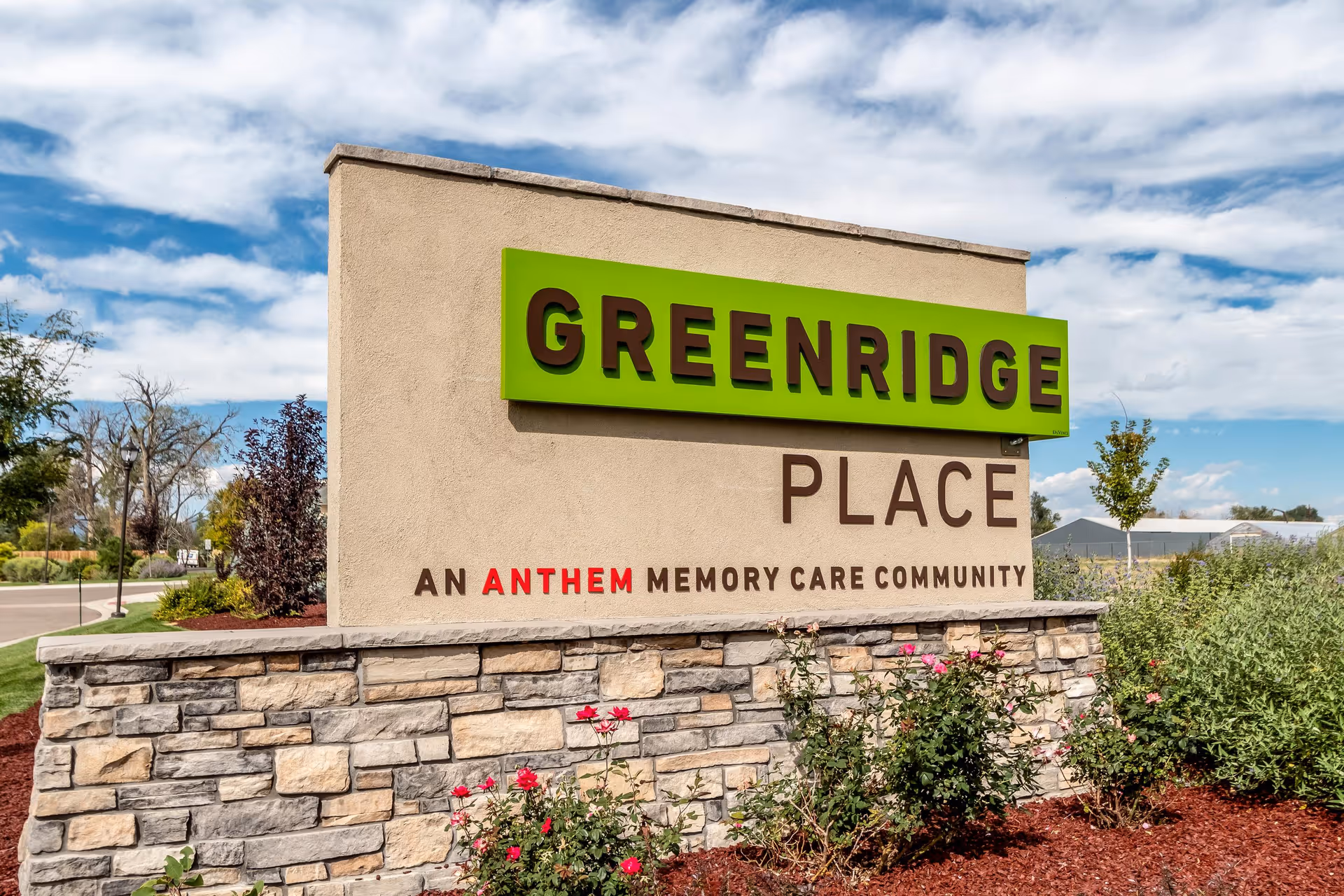 Outdoor stone and stucco sign for Greenridge Place, an Anthem memory care community, with landscaping and a partly cloudy sky in the background.