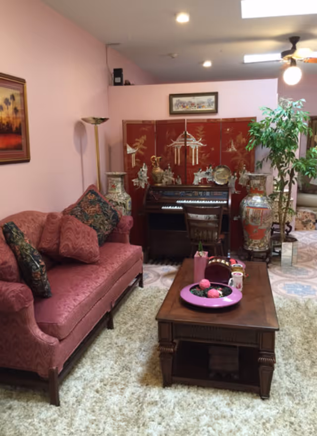 Living room with a pink upholstered sofa, wooden coffee table, decorative Asian screen, ornate vases, and a small organ.
