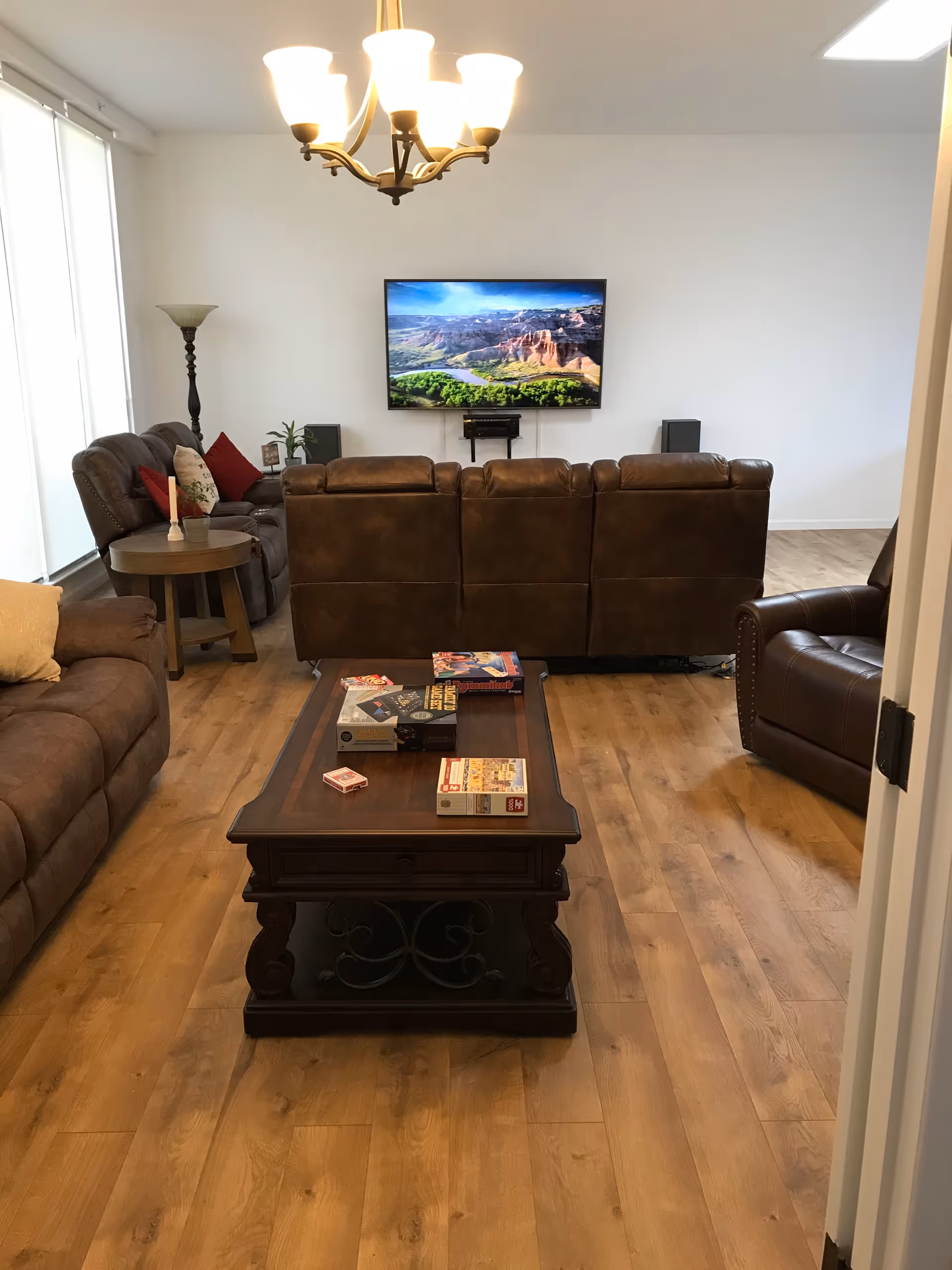 Well-lit living room with brown leather sofas facing a wall-mounted TV and a wooden coffee table on hardwood flooring.