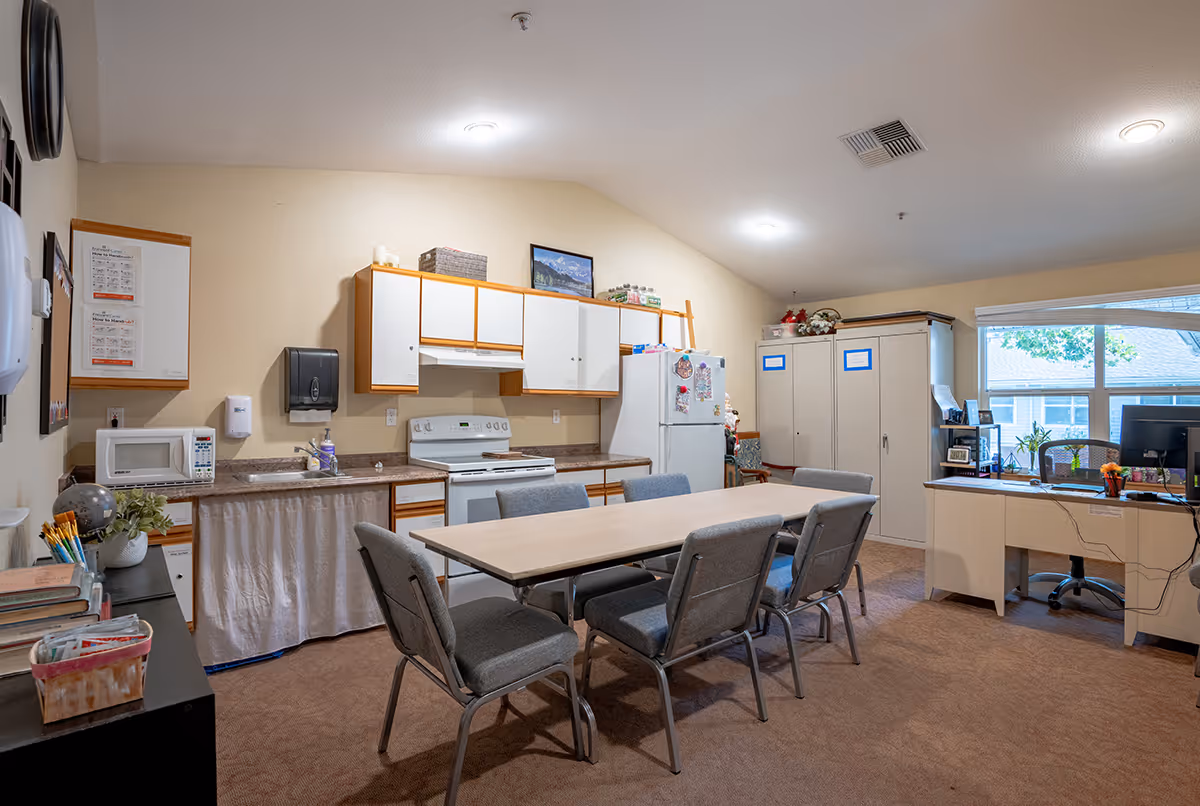 Shared dining area with a long table and kitchenette appliances along the back wall.