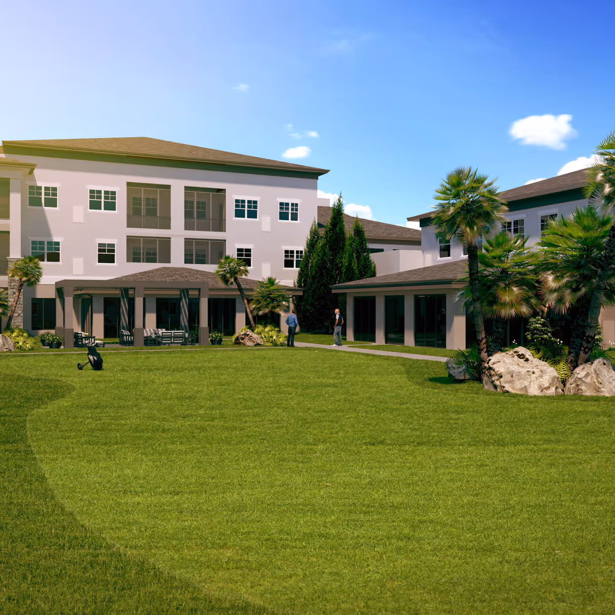 Outdoor view of a senior living facility with a large green lawn, palm trees, and two people standing on a pathway near the building under a clear blue sky.