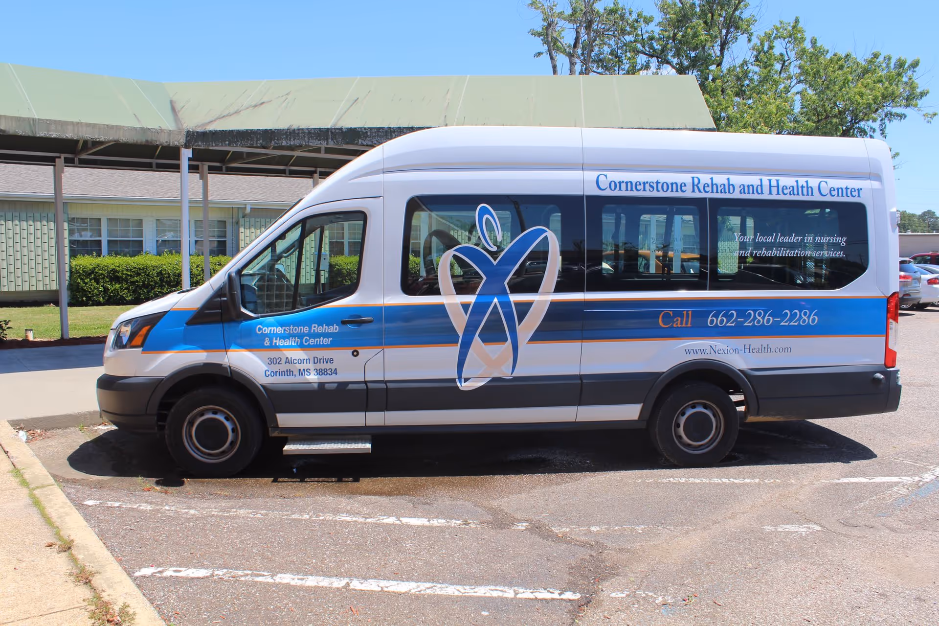 A white and blue Cornerstone Rehab and Health Center shuttle van parked in front of the facility under a green awning.