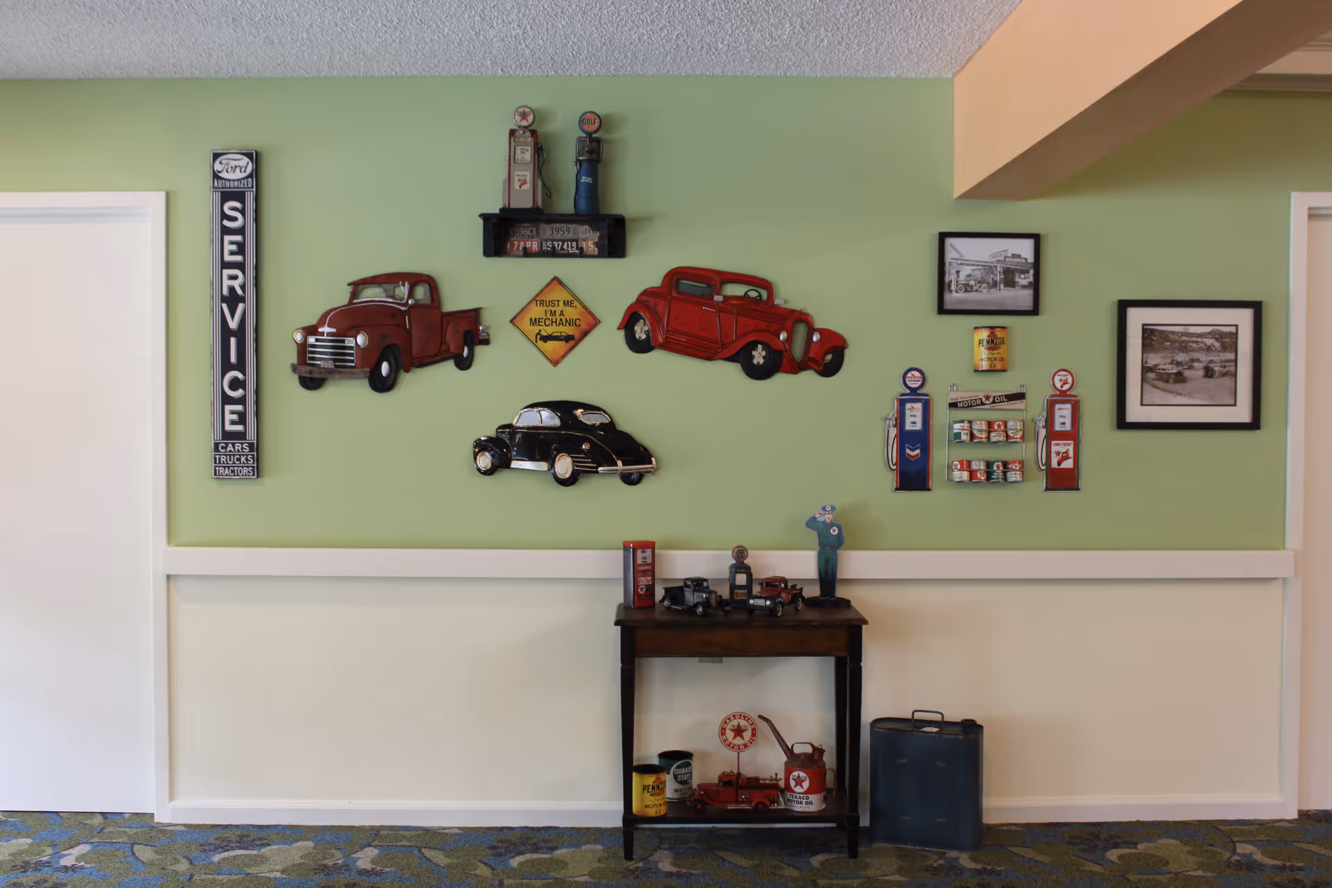 Interior wall decorated with vintage car signs, framed photos and a small table holding model cars and collectibles.