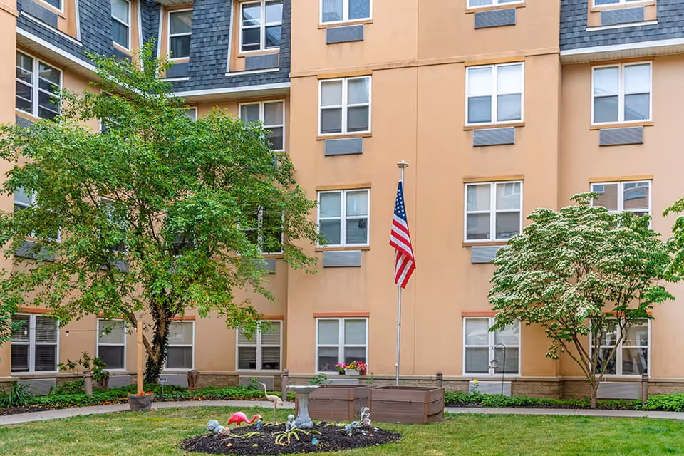 Courtyard of a multi-story senior living building with an American flag, trees, planter boxes and rows of windows.
