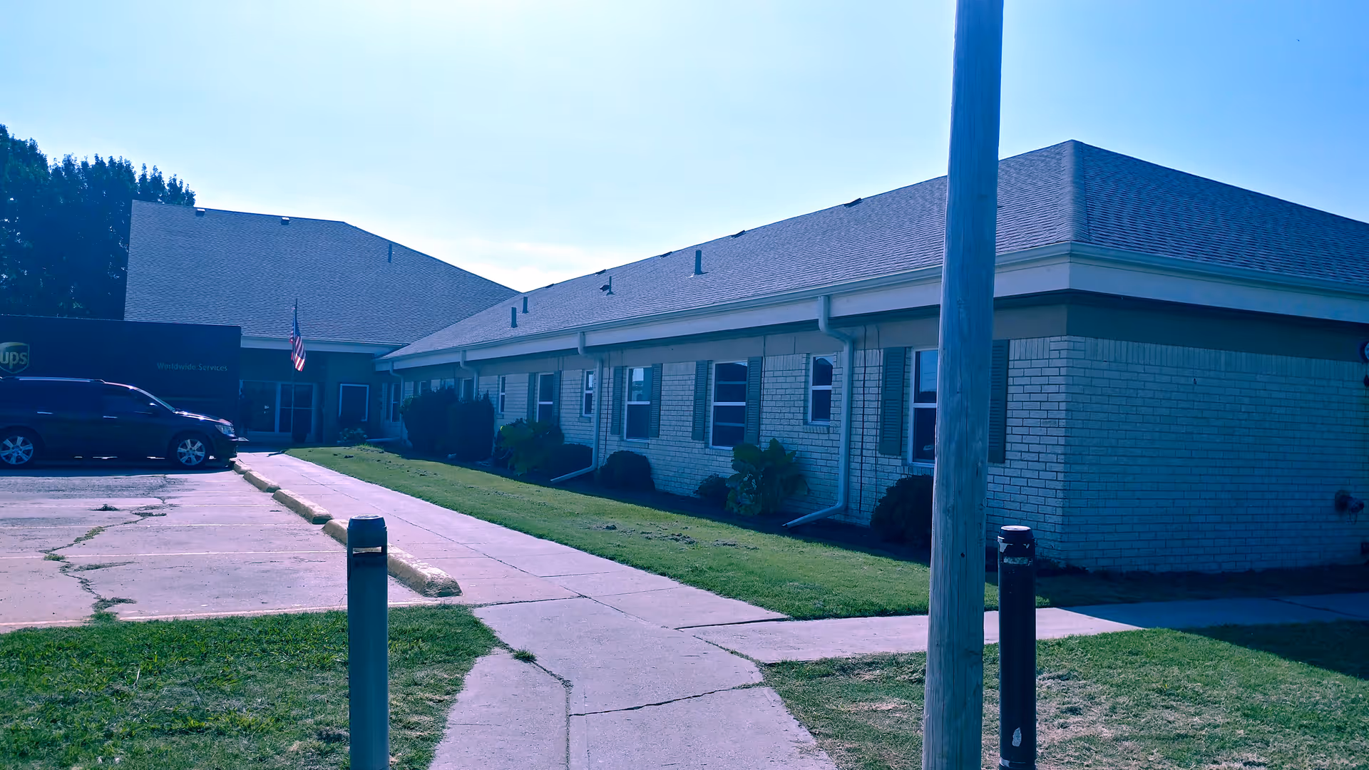 Single-story brick rehabilitation center building with a parking area, walkway, and an American flag near the entrance.