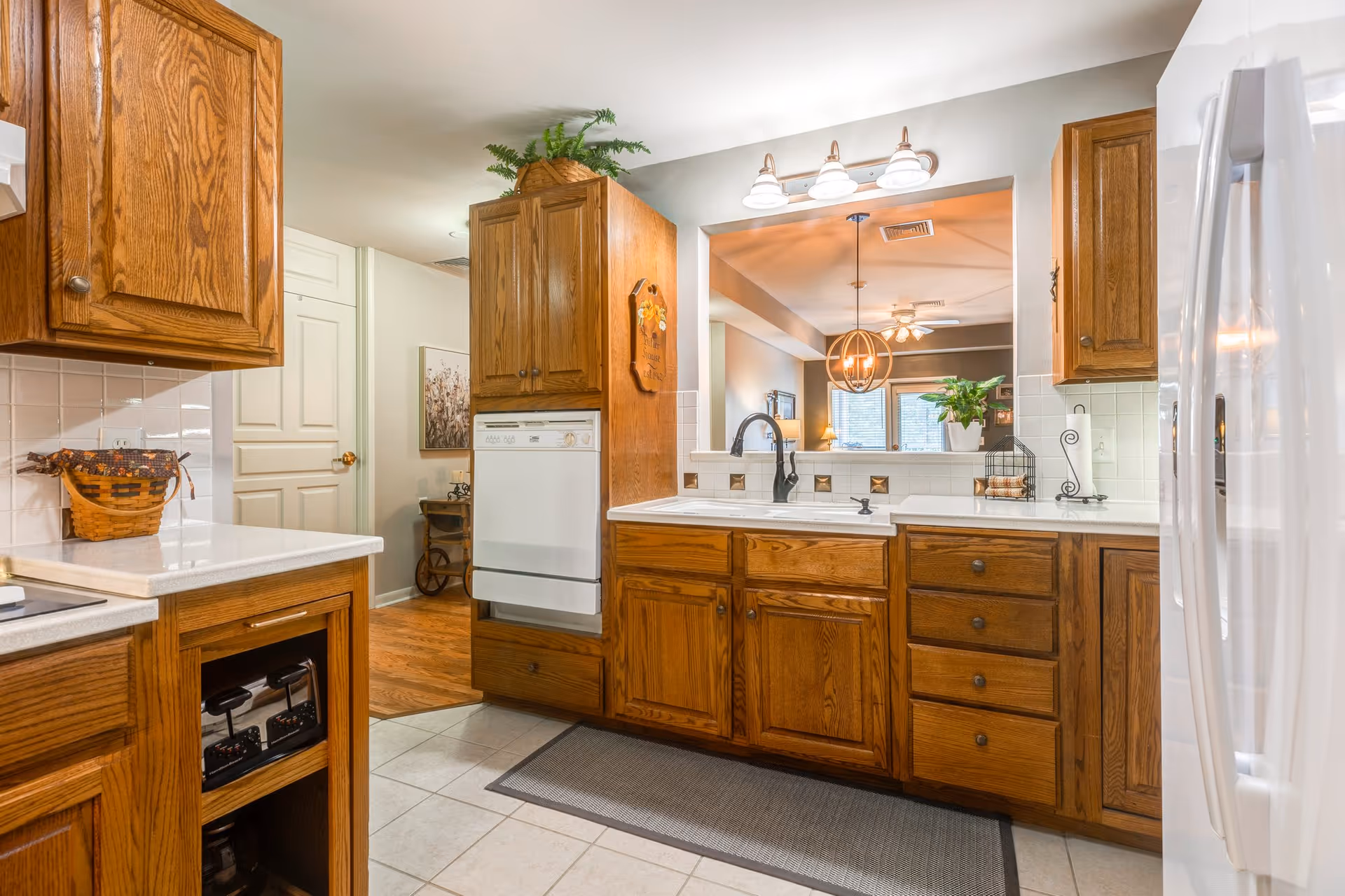 Bright kitchen with oak cabinets, white countertops, a sink beneath a passthrough to the dining area, and a white refrigerator.
