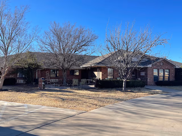 Single-story brick building front with a covered porch, leafless trees, and a driveway under a clear blue sky.
