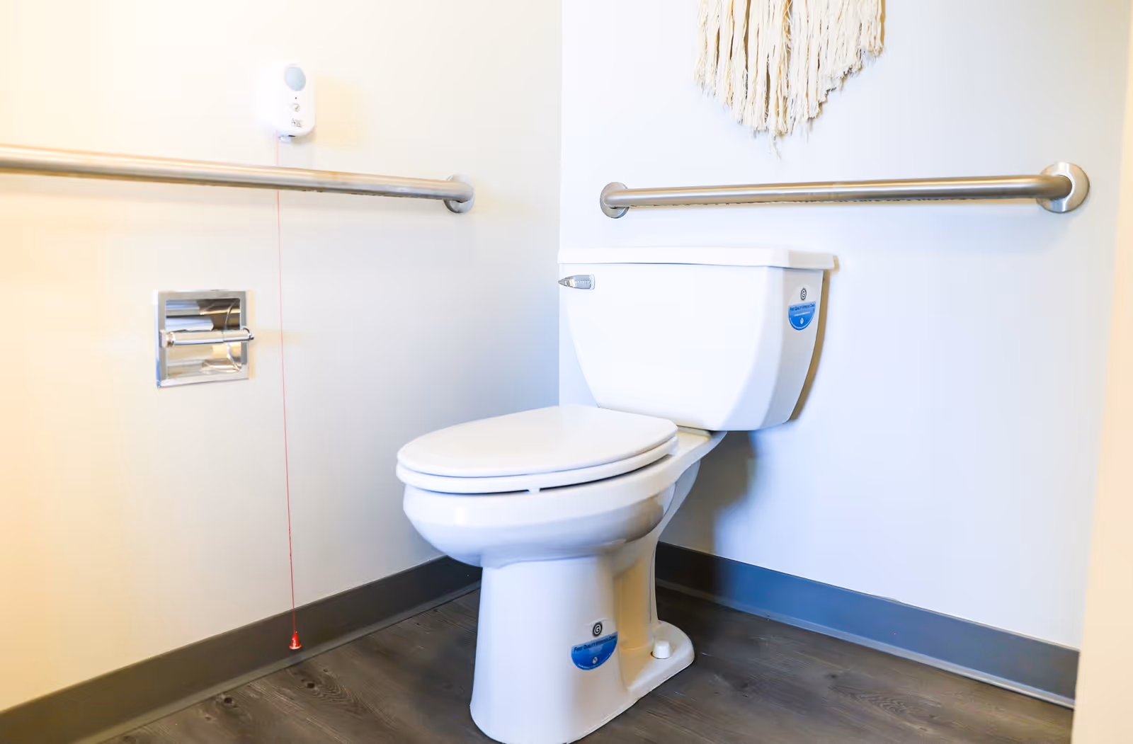 White accessible bathroom with a toilet, wall-mounted grab bars, and an emergency pull cord.