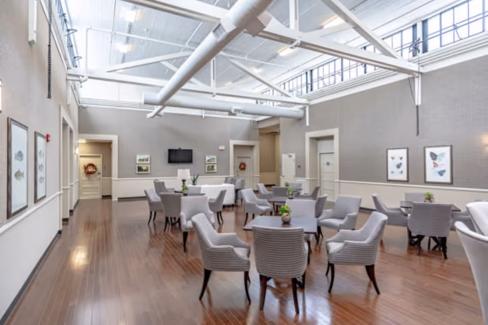 Bright communal dining/lounge area with several tables and upholstered chairs beneath skylights and exposed ceiling beams.
