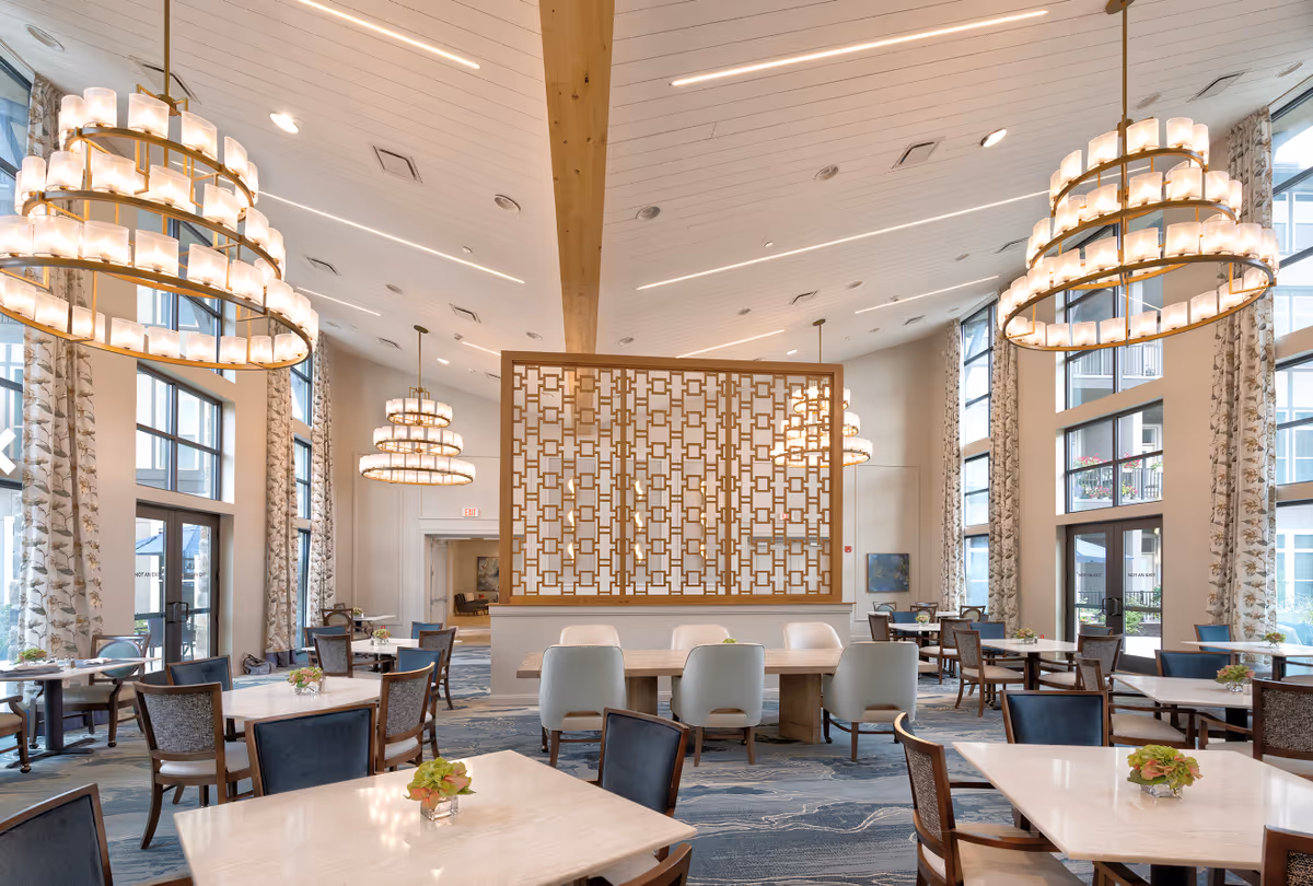 Spacious, well-lit dining room with large chandeliers, multiple tables and chairs, and a decorative wooden room divider.