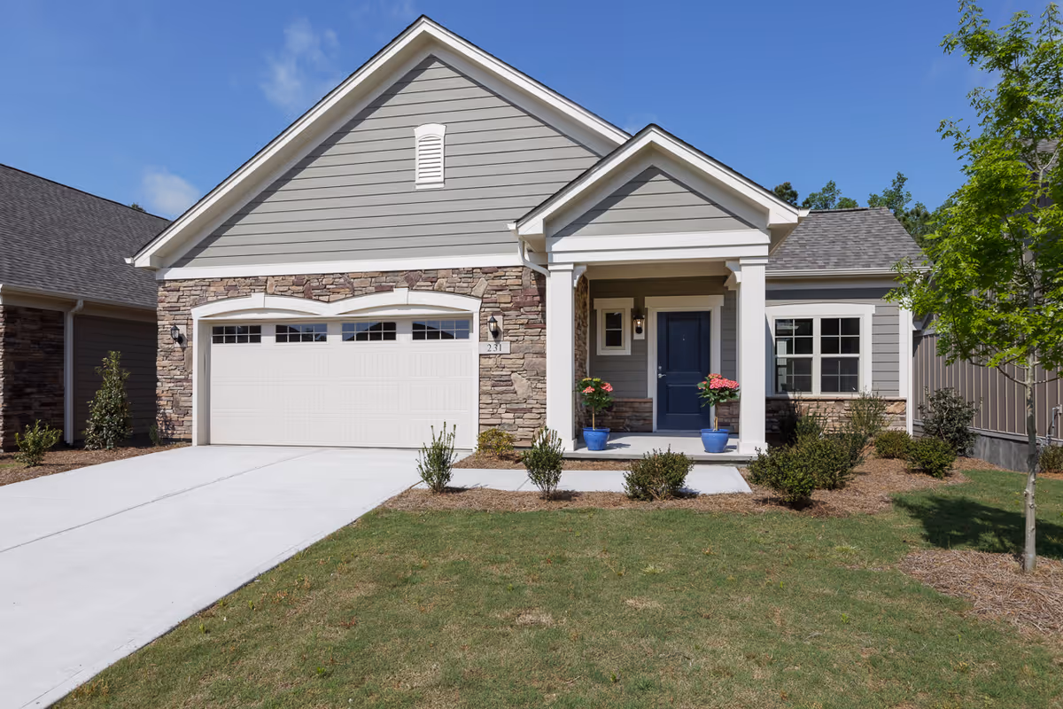 Front exterior of a single-story house with a two-car garage, blue front door, covered porch with potted flowers, and a driveway.