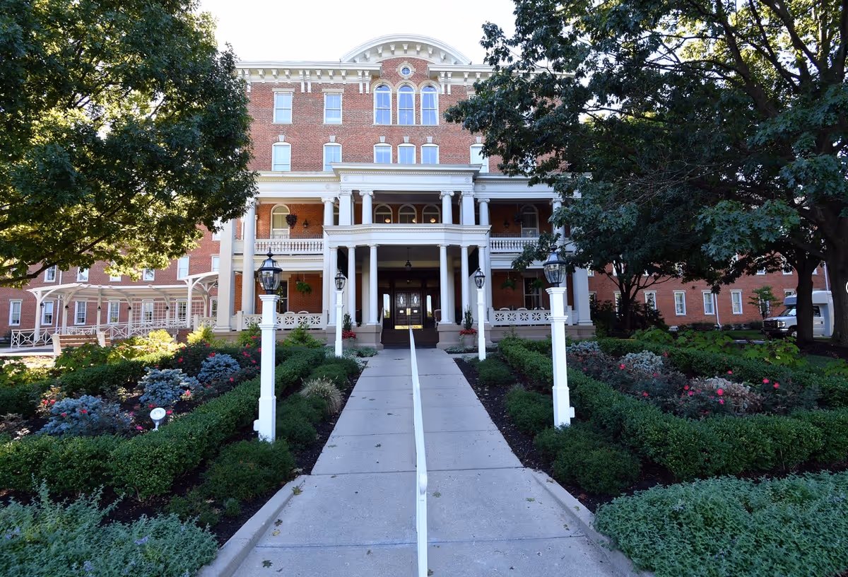 Brick senior living facility with a grand columned front entrance, walkway, and landscaped gardens