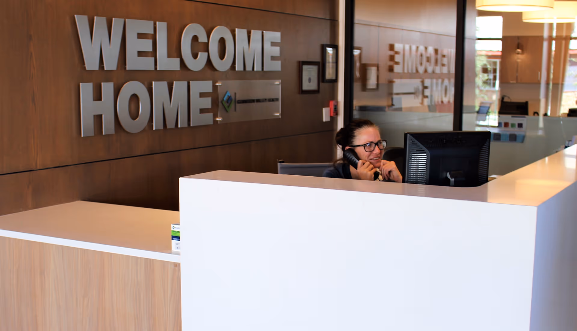 Reception desk with a large "WELCOME HOME" sign on the wall and a staff member on the phone behind the counter.