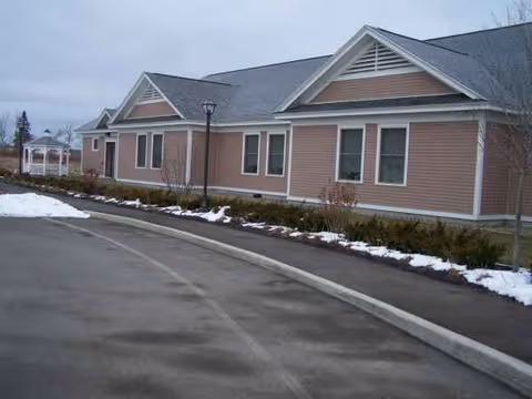 Exterior view of a single-story senior living facility with pink siding and snow along the landscaping.
