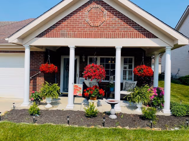 A charming entrance of a senior living facility with hanging flower baskets and potted plants.