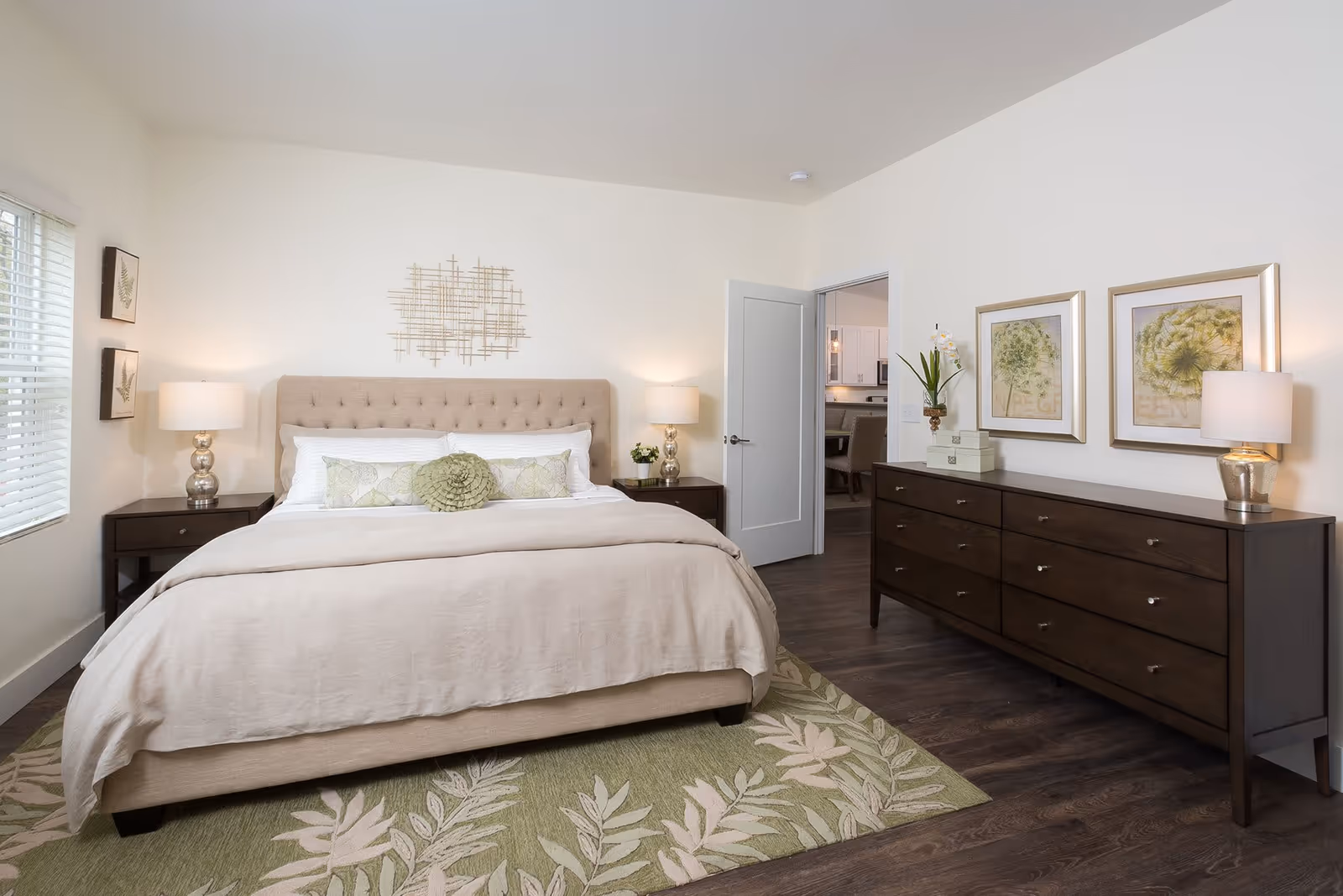 Light, neutral bedroom with a tufted bed, two nightstands with lamps, and a long dark dresser against the wall.