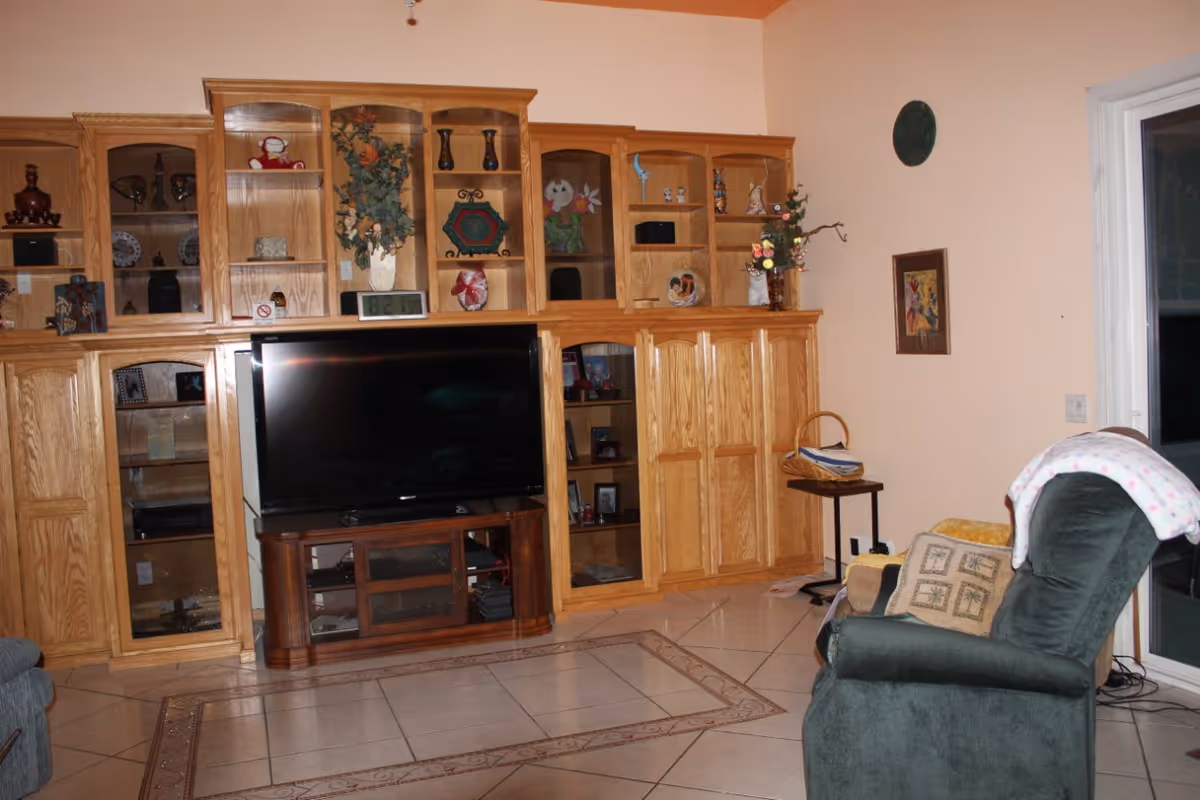 Living room with a large wooden built-in shelving unit and flat-screen TV, a green recliner, and tiled floor.