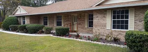 Single-story brick facility facade with windows, entry door, and neatly trimmed landscaping.