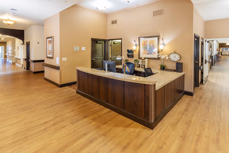 Reception desk in a senior living facility lobby with wood floors and corridors.