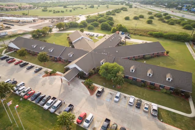 Aerial view of a single-story, star-shaped brick healthcare building with cars parked in a front lot and surrounding green lawns.