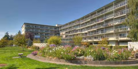 Exterior view of a multi-story senior living building with a landscaped garden in the foreground.