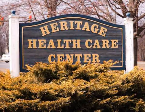Outdoor sign reading Heritage Health Care Center with yellow bushes in front