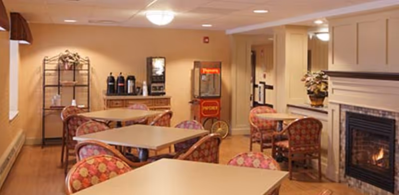 Dining room with several square tables and patterned chairs, a fireplace, beverage station and popcorn machine.
