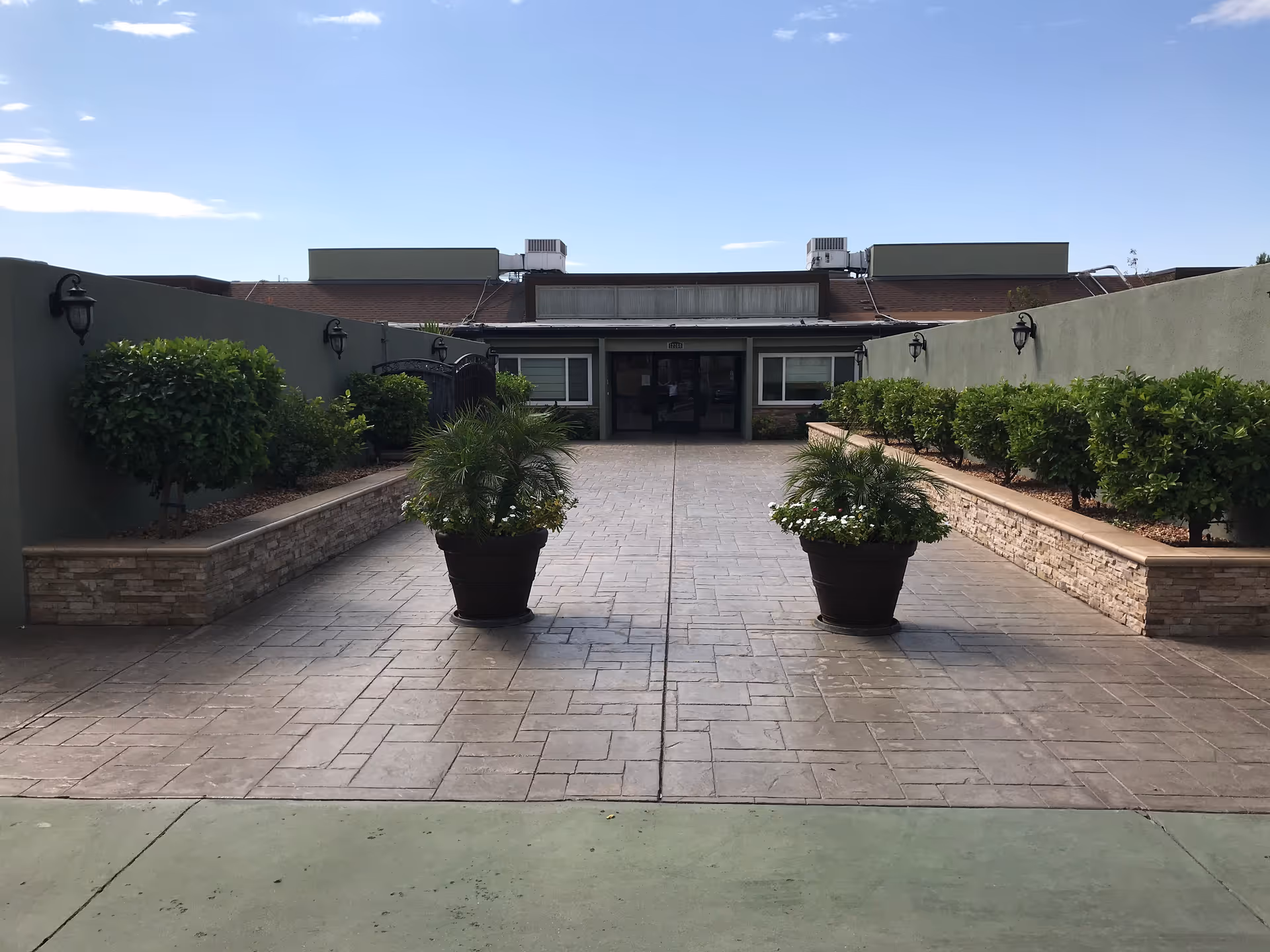 Paved courtyard with two large potted plants leading to the front entrance of a single-story building.