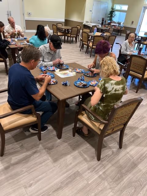 A group of residents seated around tables eating snacks in a communal dining room.