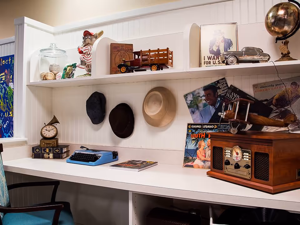 A desk and wall shelves displaying vintage decor including hats, a blue typewriter, model vehicles, records and a retro radio.