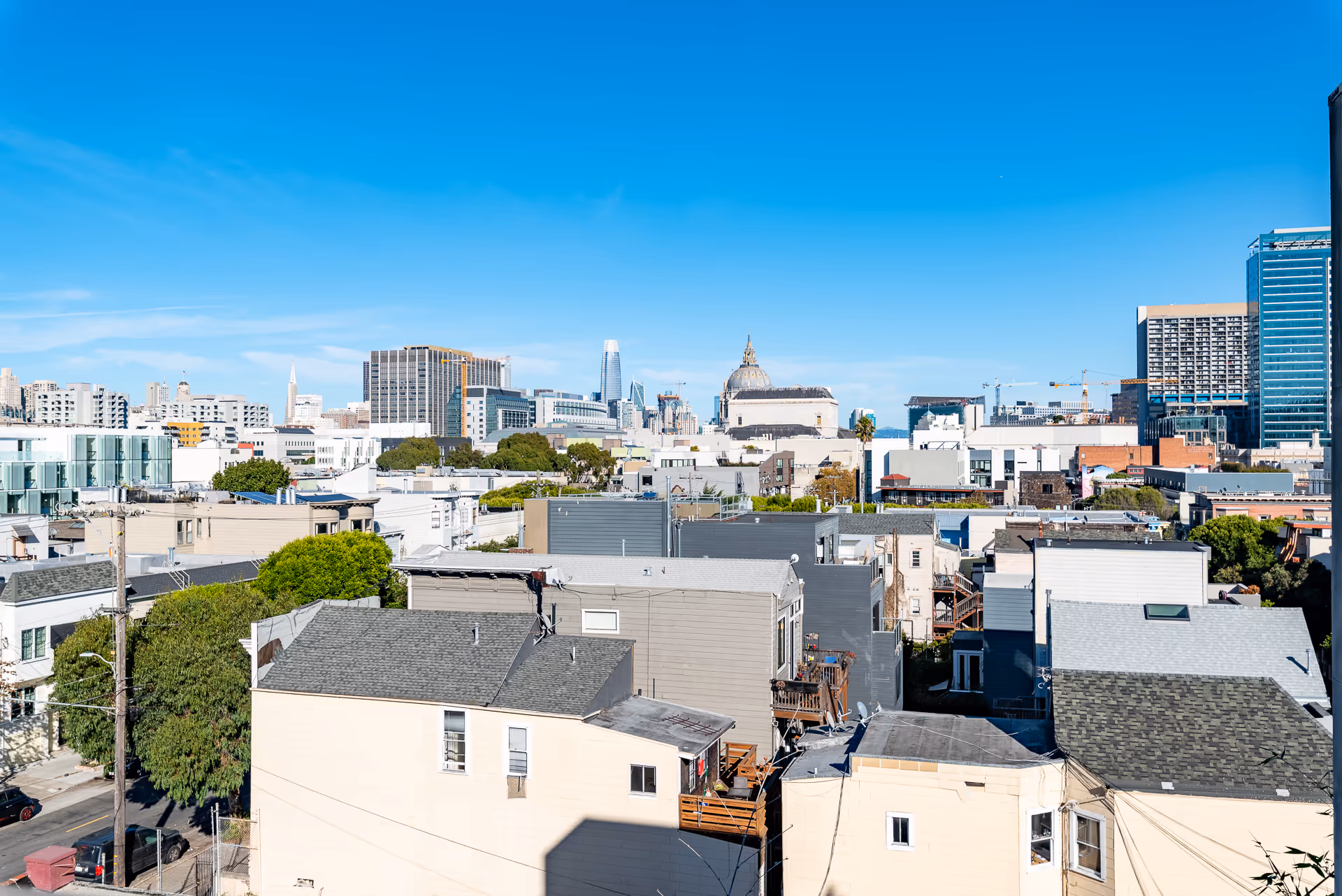 View over residential rooftops toward a city skyline under a clear blue sky.