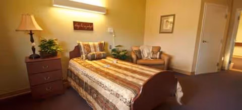 Cozy furnished bedroom at Lake Harris Inn with bed, seating area, dresser, and lamp.