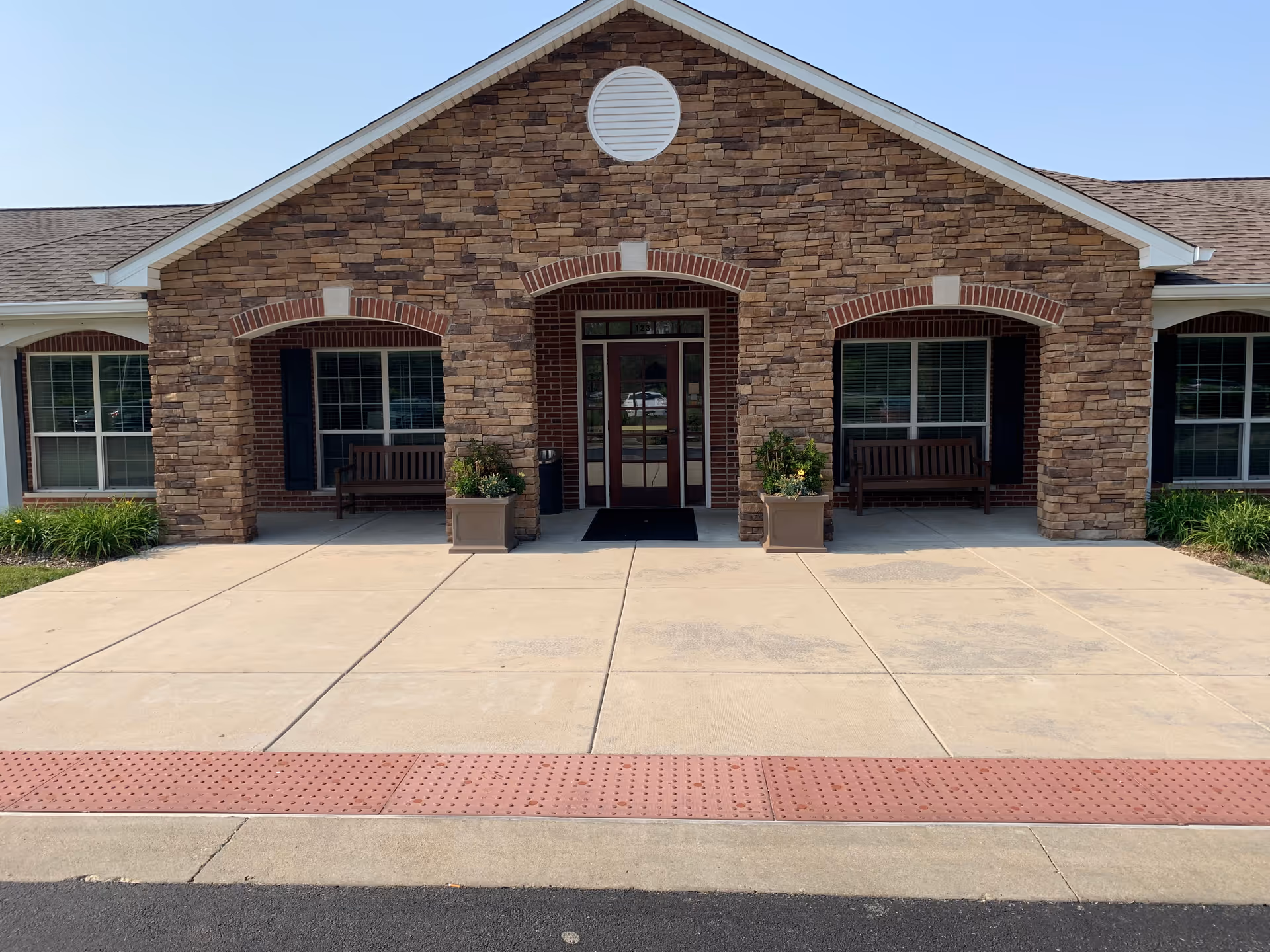 Front entrance of a stone-clad senior living building with benches and potted plants.
